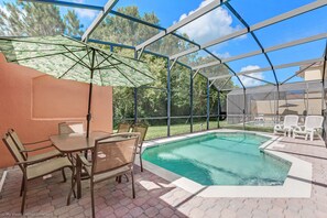 A covered outdoor swimming pool with a glass enclosure, a table with chairs, and a patio area with lounge chairs. - Vero Beach Villa Terra Verde (Kissimmee)