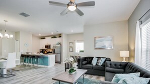 A modern living room with a grey sofa, a coffee table, and a dining area with white chairs. - Slice Way Villa Champions Gate 1 (Davenport)