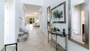 Un intérieur moderne avec un escalier menant à un espace repas, une console en verre agrémentée d’un miroir et une œuvre d’art encadrée accrochée au mur.