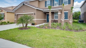 A two-story house with a beige exterior, a dark blue garage door, and a well-maintained front yard with grass and palm trees. - Oakbrone Avenue Villa Solterra 3 (Davenport)