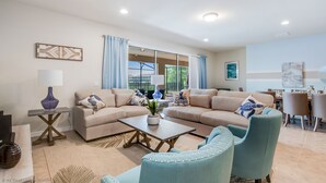 A living room with a beige sofa, a coffee table, and a dining area with a table and chairs. - Bengal Court Villa Windsor at westsdie 8805 (Kissimmee)