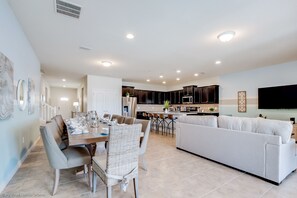 A modern open-plan living area with a dining table, sofas, and a kitchen in the background. - Bengal Court Villa Windsor at westsdie 8805 (Kissimmee)