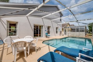 Ein überdachter Poolbereich mit Tisch und Stühlen, eine überdachte Terrasse und im Hintergrund der Blick auf das Haus.