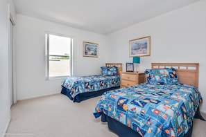 A bedroom with two beds, a dresser, and two framed pictures on the wall.