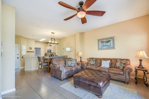 A spacious living room with a ceiling fan, two sofas, a coffee table, and a dining area with a chandelier.