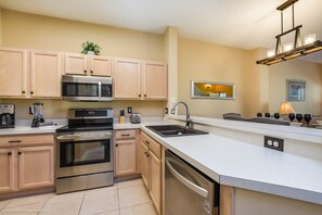 A modern kitchen with stainless steel appliances, wooden cabinets, and a white countertop.