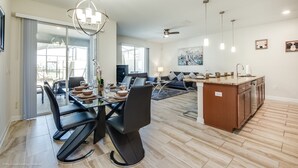 Uma sala de estar espaçosa com uma mesa de jantar, cadeiras pretas, uma ilha de cozinha e uma grande janela que proporciona iluminação natural.