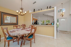 A dining area with a table set for four, surrounded by wooden chairs with blue cushions. A chandelier hangs above the table, and a large mirror is mounted on the wall. - 234glen Fantastically Decorated 4 bed 2 Bath (Davenport)