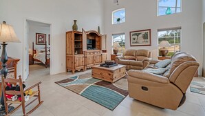 A spacious living room with a large ceiling fan, a leather sofa, a wooden cabinet, and a bed in the background. - 234glen Fantastically Decorated 4 bed 2 Bath (Davenport)