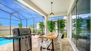 An outdoor patio with a grill, dining table, chairs, and potted plants. - 1560npt New Solara 9 Bedroom 6 Bathroom Resort (Kissimmee)