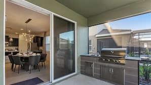 A modern kitchen with a sliding glass door leading to a dining area, a built-in grill, and a view of the backyard.