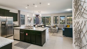 A modern kitchen with a central island, stainless steel appliances, pendant lighting, and a view to a living area with a sofa and a coffee table.