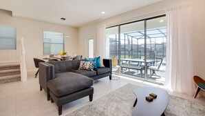 A modern living room with a gray sectional sofa, a coffee table, and a dining area with a glass-top table. - 8916sydney Fantastic 5 Bed 4 Bathroom Town Home (Kissimmee)