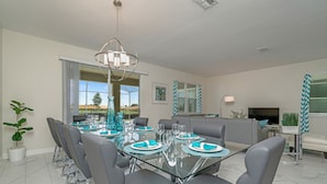 A modern dining area with a glass table, grey chairs, and teal accents. - 891pbeach Amazing Champions Gate 9 Bedroom 5 Bed (Davenport)
