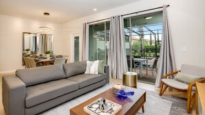A modern living room with a grey sofa, a wooden coffee table, and a dining area with a glass door leading to an outdoor patio.
