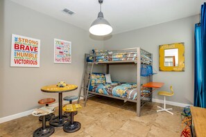 A bunk bed with a Minion-themed bedspread, a small round table with stools, a chair, and a mirror on the wall. - Rolling Fairway Villa Champions Gate 2 (Davenport)