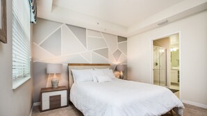A bedroom with a bed, nightstands, a geometric wall design, a window with blinds, and a bathroom visible through an open door. - 4741ct Unit101 Amazing Story Lake Brand New Condo (Kissimmee)