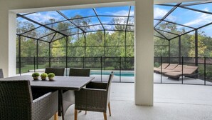 A covered patio with a table and chairs, a pool, and lounge chairs. - 518mb New and Modern 8 Bedroom 5 Bathroom Villa (Kissimmee)