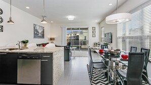 Una cocina moderna con lavavajillas, un comedor con una mesa larga y sillas, y vistas al exterior a través de un ventanal.