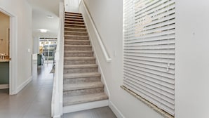 Una escalera con peldaños alfombrados y barandillas blancas, que conduce a un rellano con vistas a una zona de cocina.