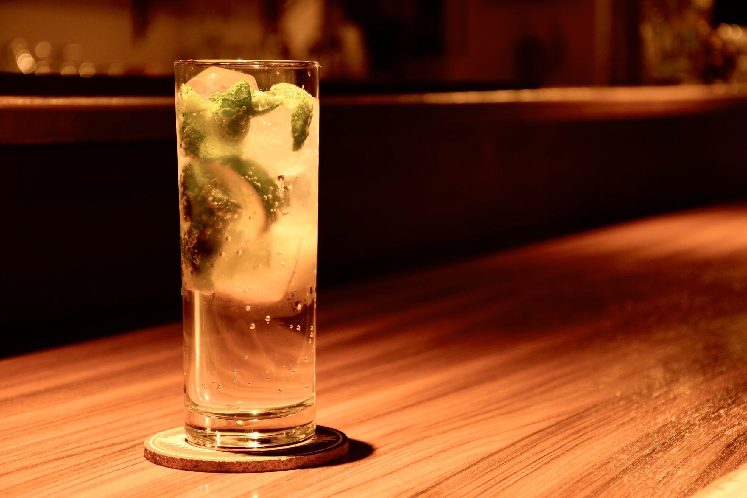Un vaso de agua con hielo y hojas de menta sobre un posavasos de madera.
