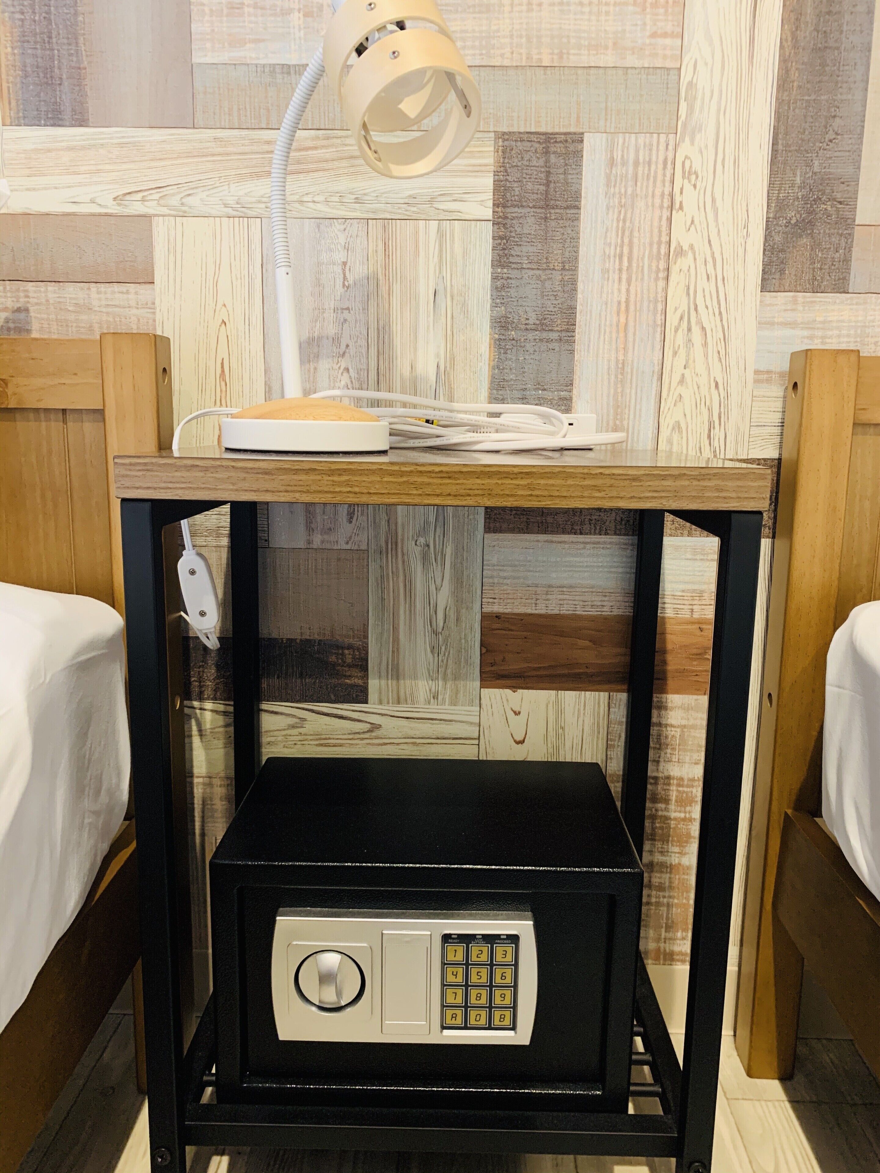 A compact room with a bed, a bedside table with a lamp, and a small safe.