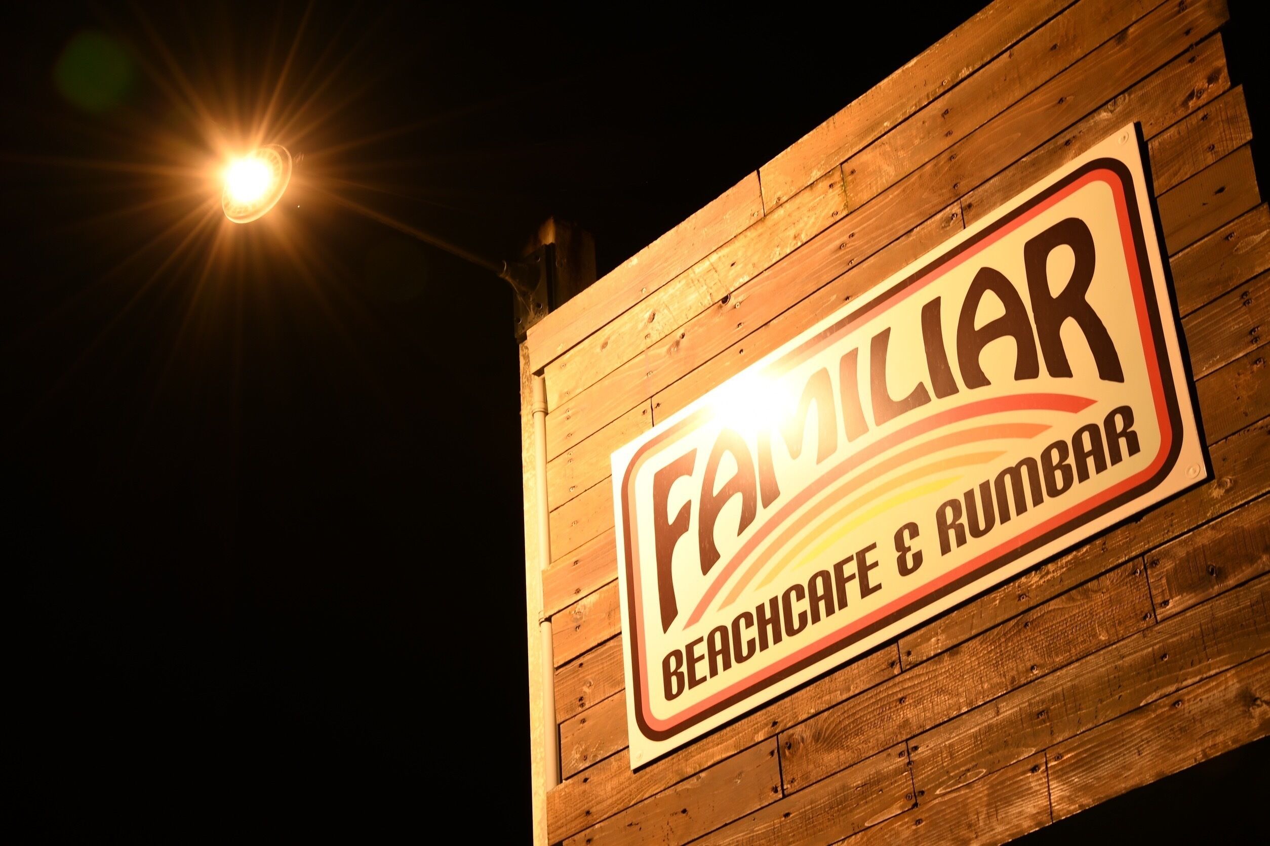A sign for 'Familiar Beach Cafe & Rumbar' against a wooden wall.