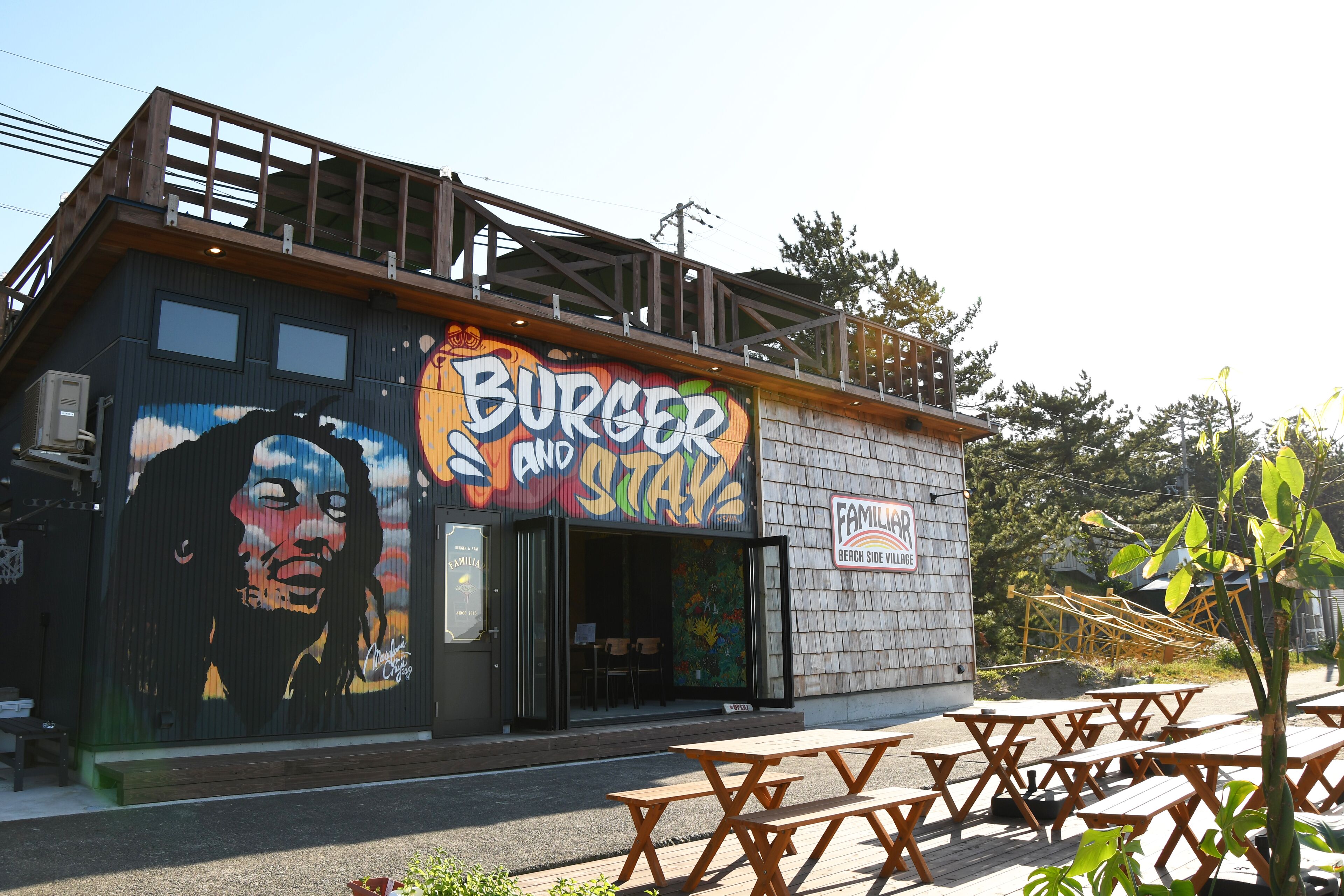 A building with a mural, outdoor seating, and a sign that reads "Burger and Stay".