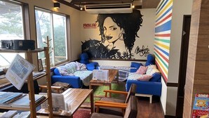 A cozy reading area with blue sofas, a wooden table with books, and a large mural on the wall. - Beach Side Village Familiar - Hostel (Takahama)