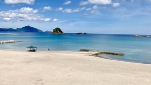 A beach with clear blue water, a small island, and a lighthouse in the distance. - Beach Side Village Familiar - Hostel (Takahama)