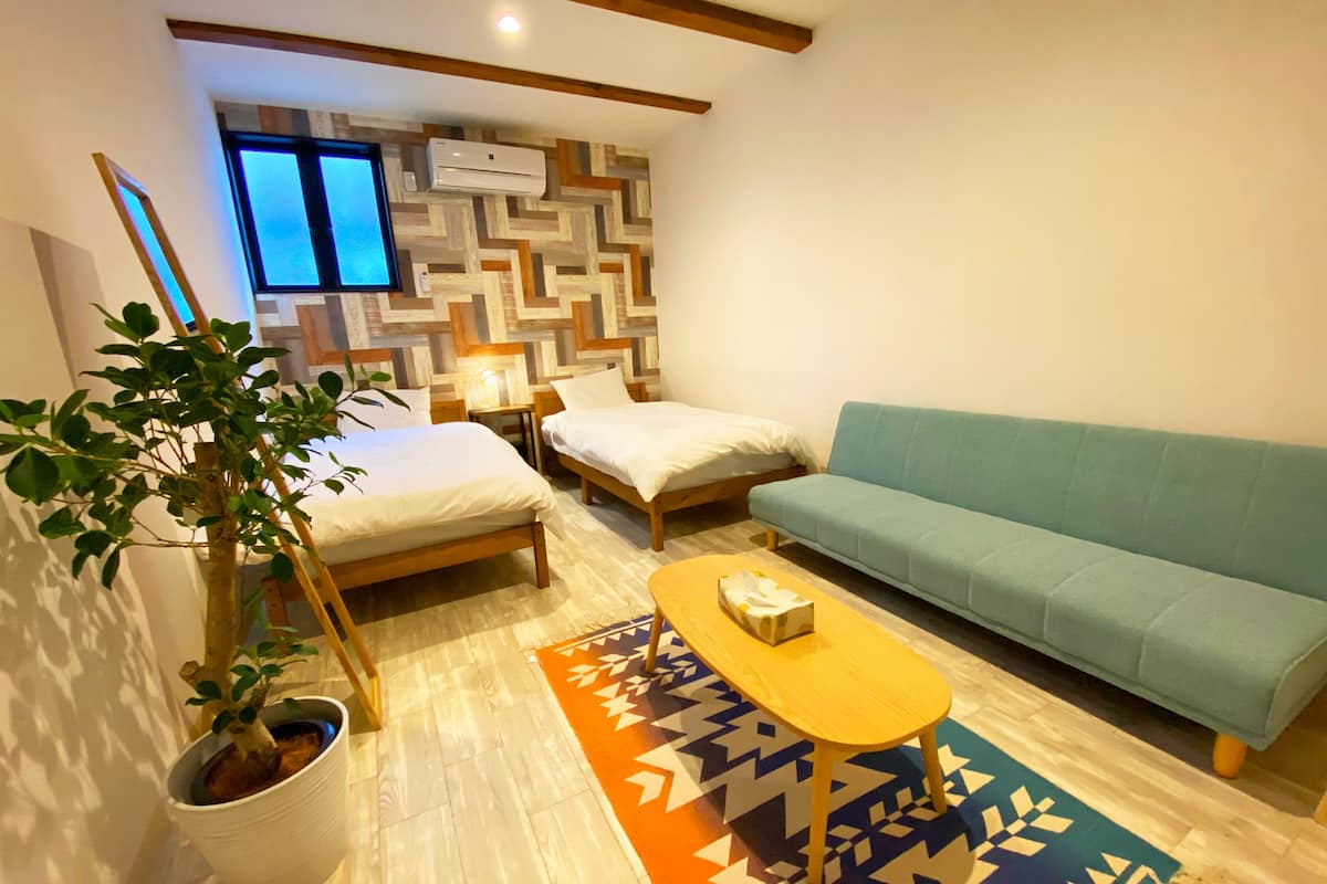 A small, cozy room with two beds, a sofa, a coffee table, and a potted plant.