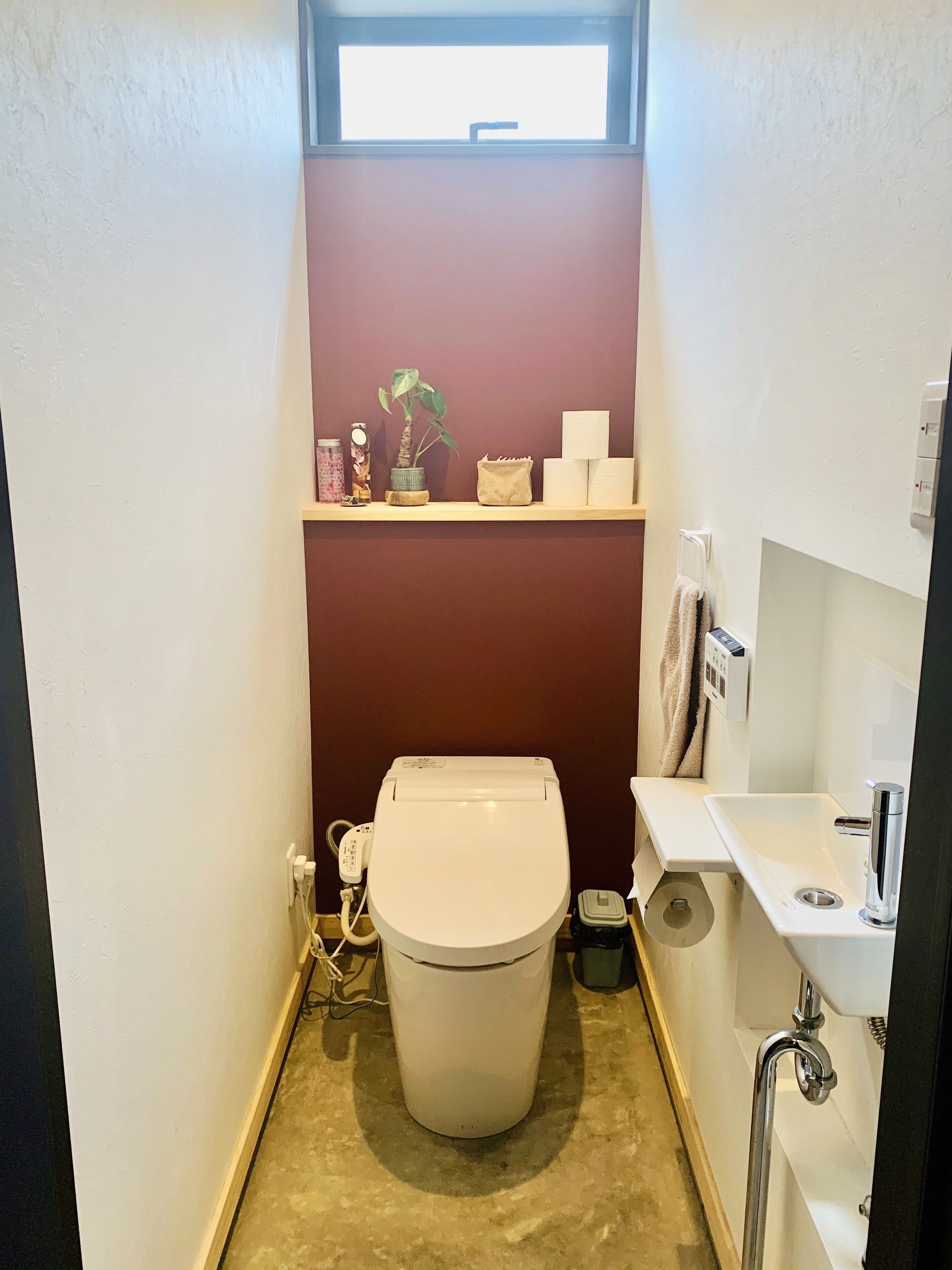 A compact bathroom with a toilet, sink, and a small shelf with toiletries.