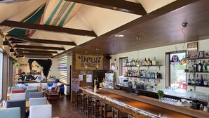 A bar area with a wooden bar counter, stools, and a mural on the wall. - Beach Side Village Familiar - Hostel (Takahama)