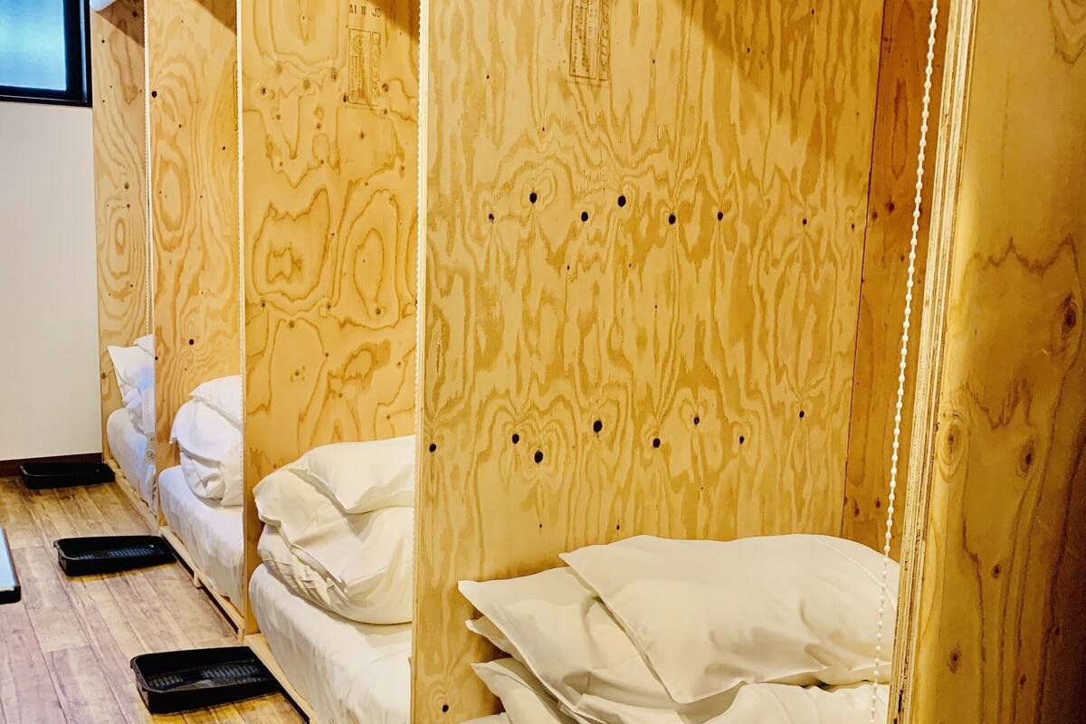 A row of wooden bunk beds with white bedding and black mats on a wooden floor.