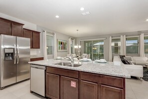 A modern kitchen with stainless steel appliances, a granite countertop, and a dining area with a white sofa. - Oakwood Street Villa Solterra 1 (Davenport)