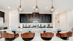 A modern kitchen with dark cabinets, a central island with bar stools, and pendant lighting.