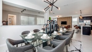 A modern dining area with a glass table, grey chairs, and a black chandelier.