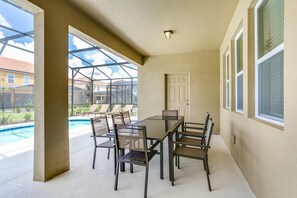 A covered patio with a glass table and chairs, a door, and a view of a swimming pool.