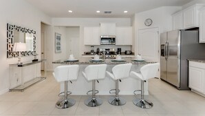 A modern kitchen with white cabinets, stainless steel appliances, and a central island with bar stools. - Oakwood Stree Villa Solterra 7041 (Davenport)
