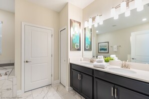 A modern bathroom with a double sink vanity, a large mirror with lights, and a door.