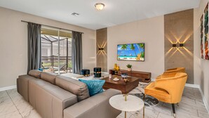 A modern living room with a beige sofa, a coffee table, and a TV on the wall. - Bookmark Villa Storey Lake (Kissimmee)