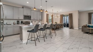 A modern kitchen with grey cabinets, a central island with bar stools, and pendant lighting. - Bookmark Villa Storey Lake (Kissimmee)