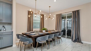 A modern dining area with a long table, multiple chairs, and pendant lighting. - Bookmark Villa Storey Lake (Kissimmee)