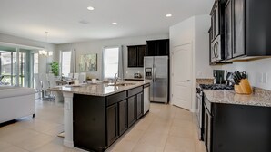 A modern kitchen with a large island, dark cabinets, stainless steel appliances, and a view to the dining area.