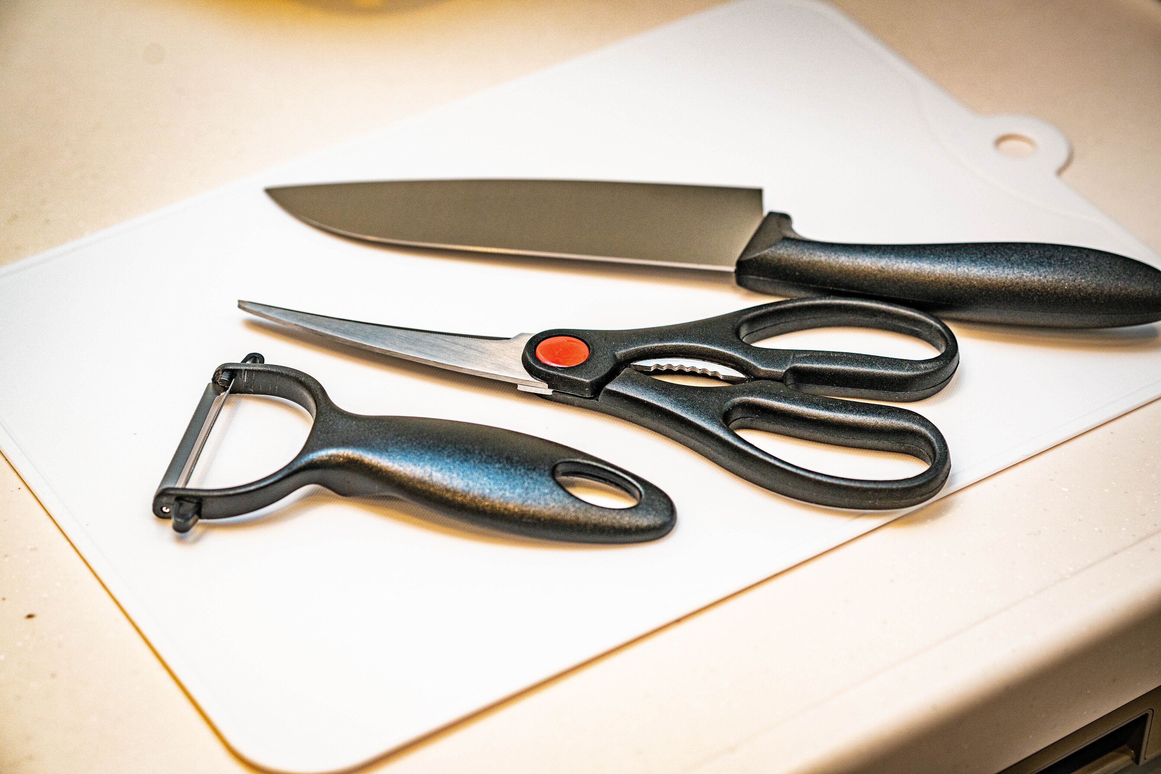 A pair of scissors and a knife on a white cutting board.