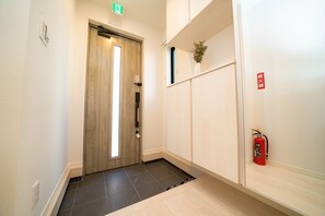 A hallway with a wooden door, a fire extinguisher, and a small plant on a shelf. - Tachibana House (Tokyo)