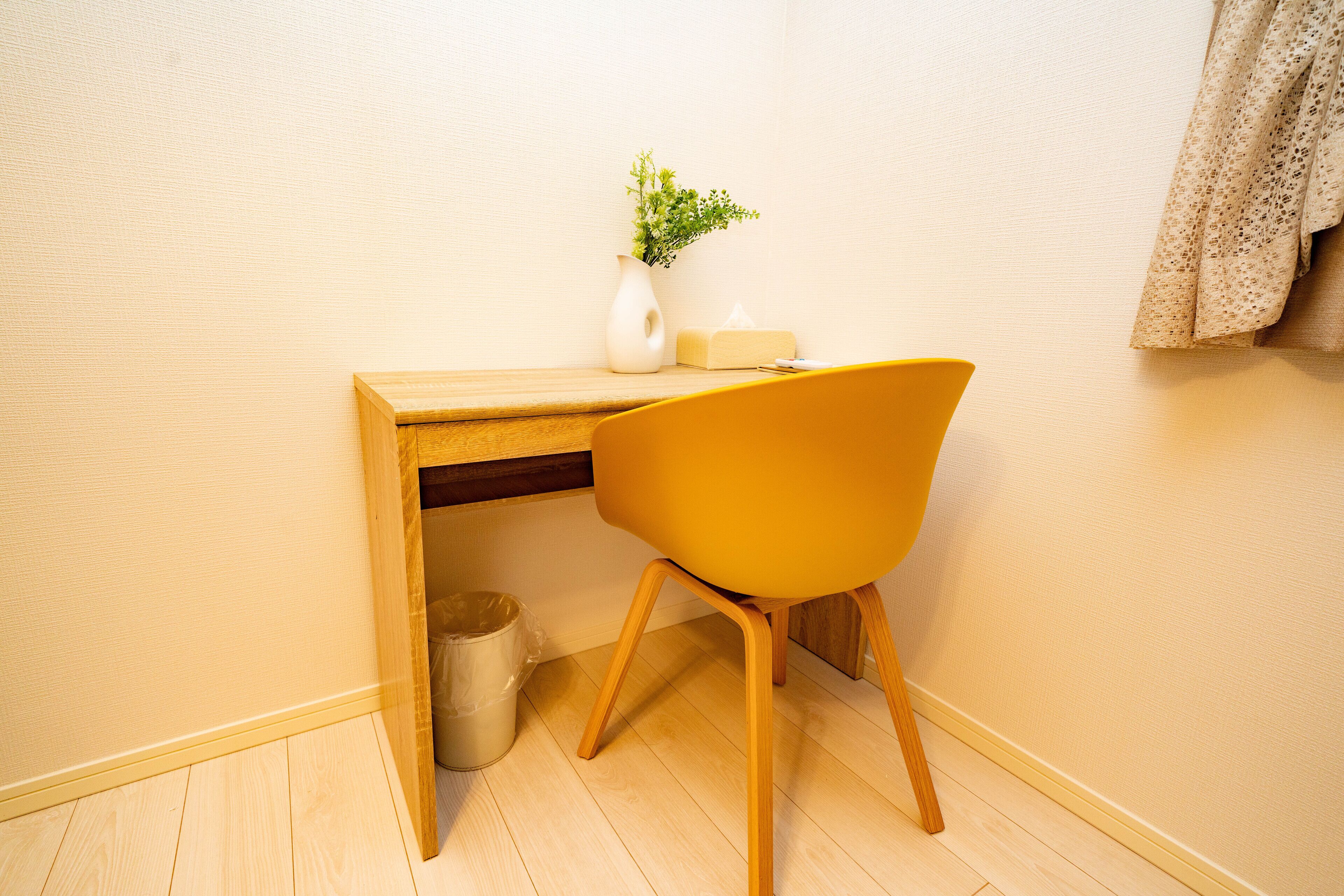 Una scrivania in legno con una sedia gialla, un vaso con piante verdi e un portatovaglioli.