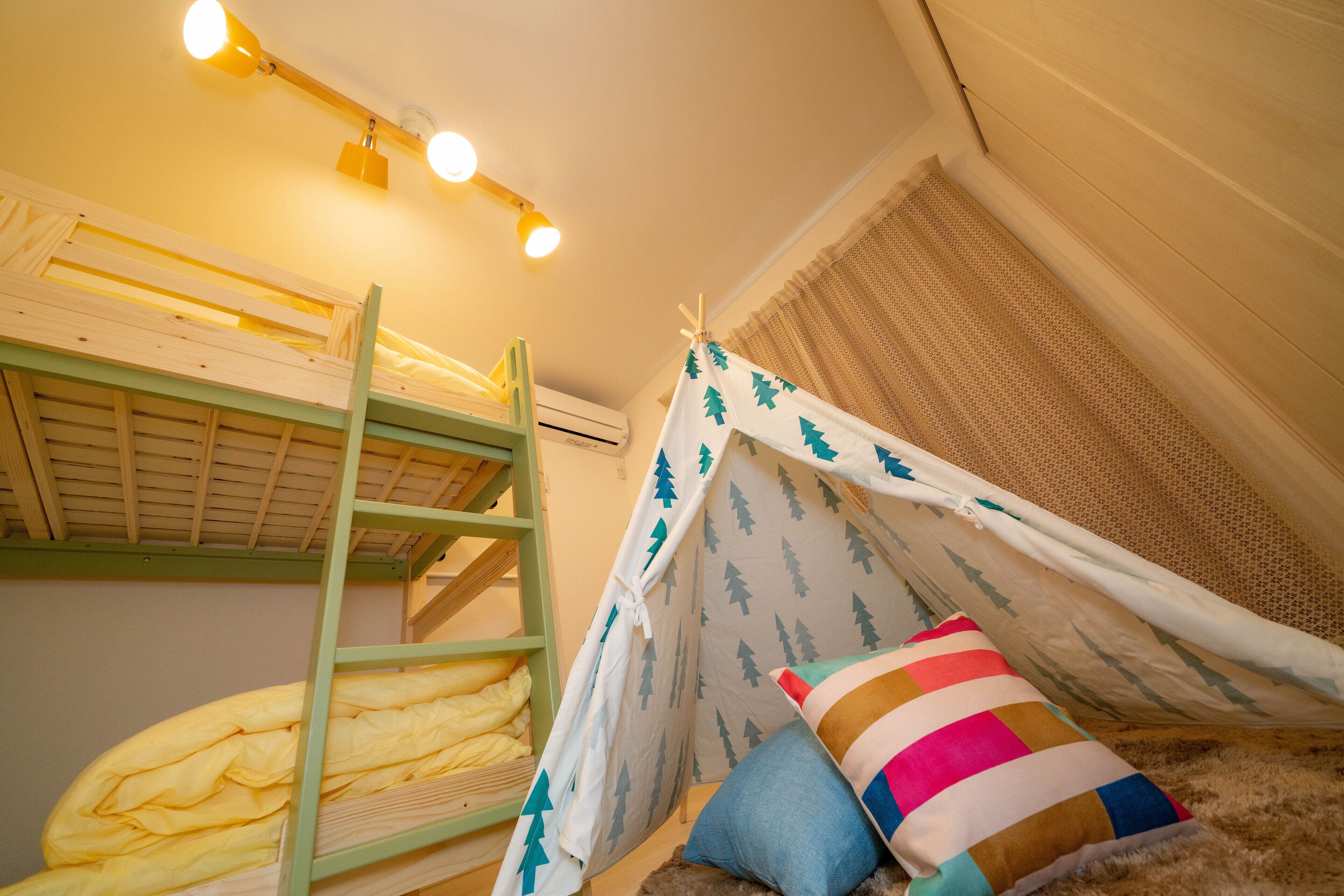Un lit superposé avec une structure verte, un ciel de lit blanc orné de motifs d’arbres et un coussin rayé aux couleurs vives.