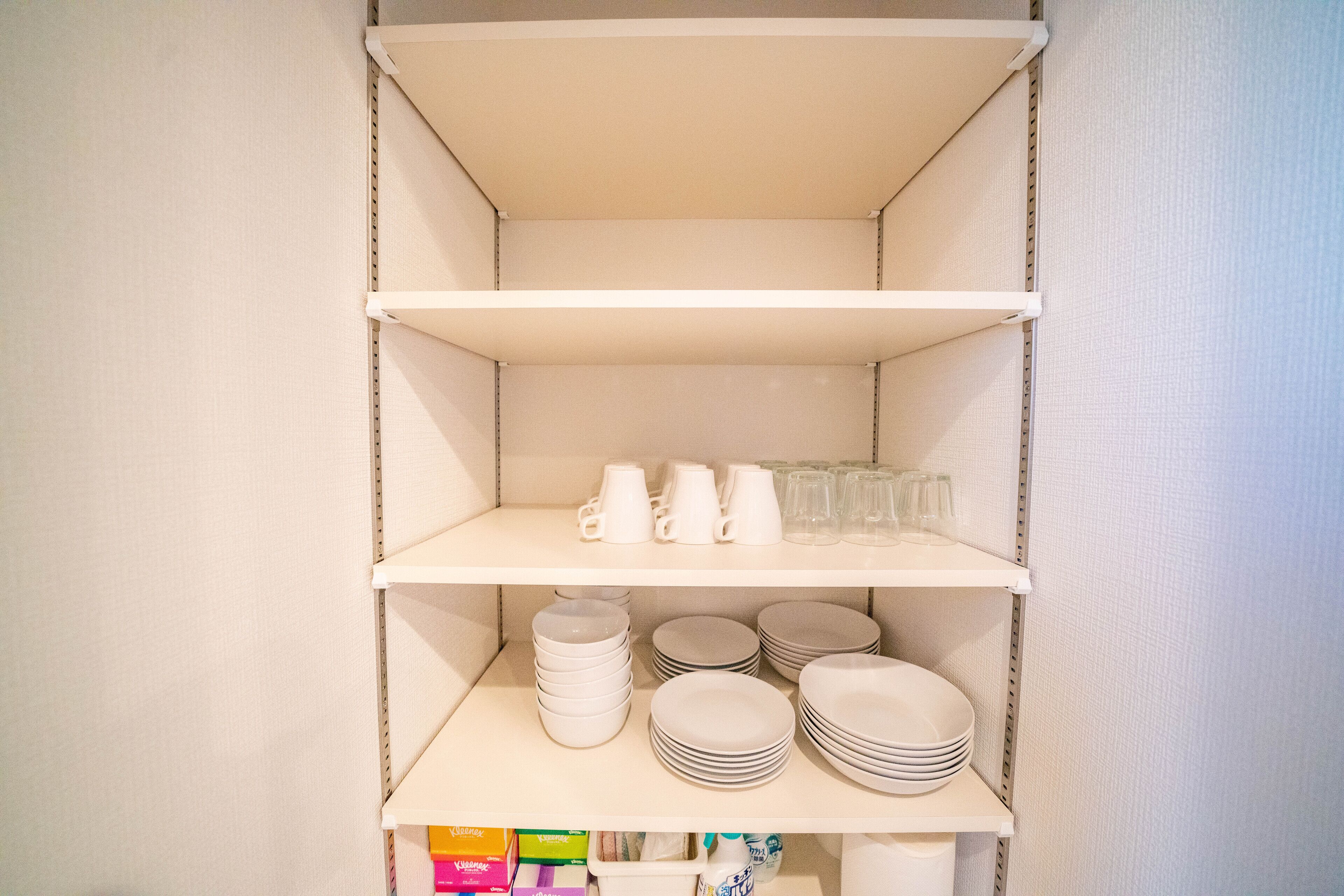 A storage unit with shelves containing white mugs, glasses, and plates.