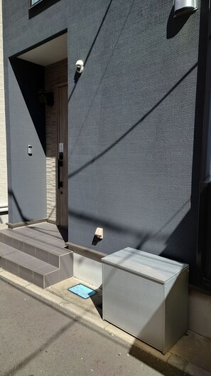 A building facade with a textured pattern, a door, and steps leading to a covered entrance. - Tachibana House (Tokyo)